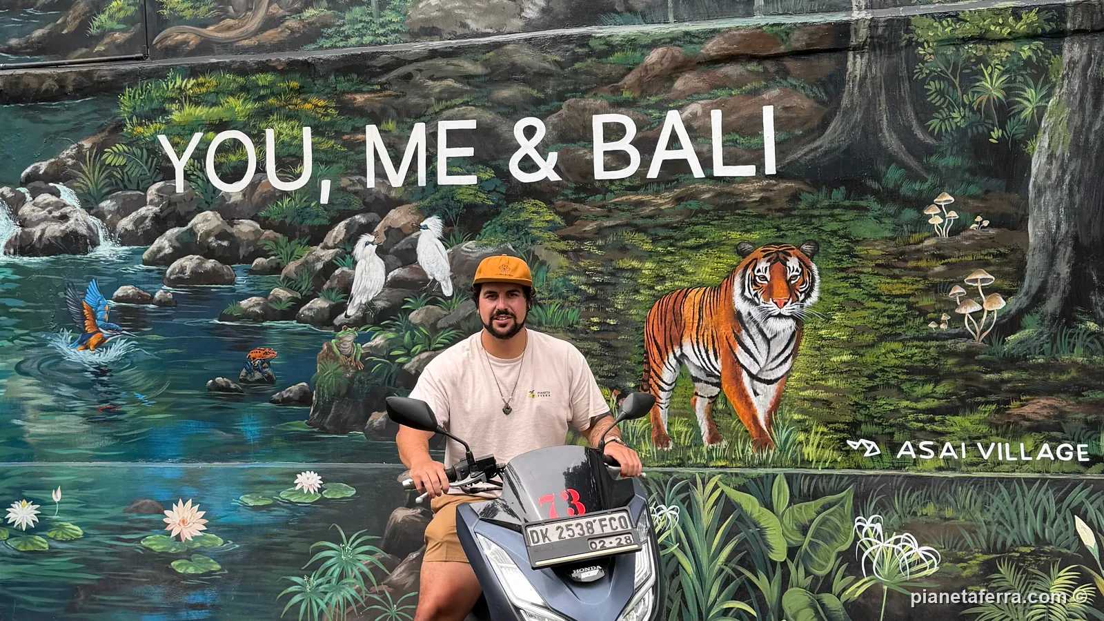 Luca sullo scooter a noleggio davanti a un murale con la scritta You, Me and Bali