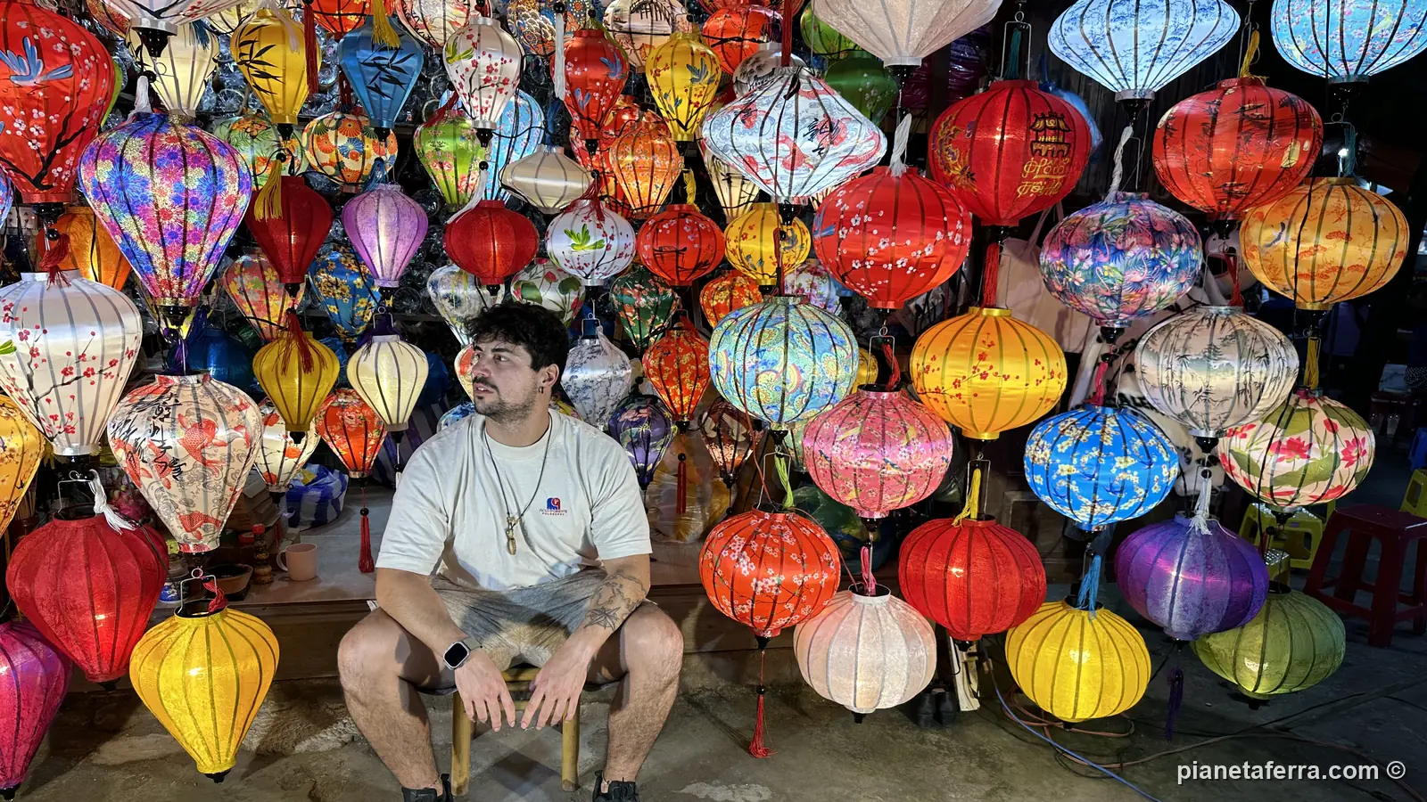 Un muro di lanterne colorate nel centro storico di Hoi An, con un viaggiatore seduto davanti
