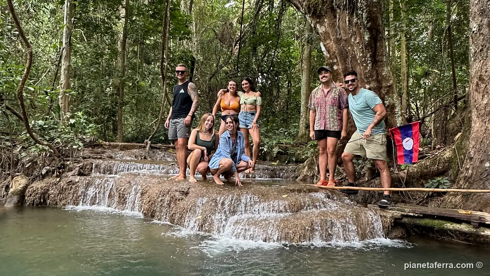 Luca con i ragazzi conosciuti in viaggio e la bandiera del Laos sulle vasche basse di Kuang Si
