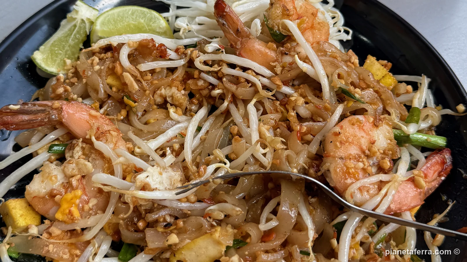 Un piatto di pad thai con i gamberi, lime e arachidi su un tavolo del mercato di Chatuchak