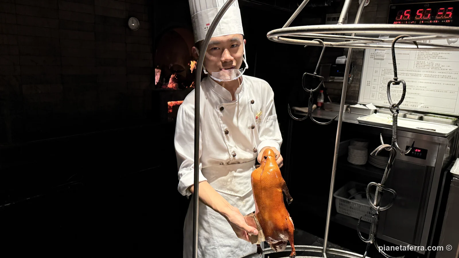 Il cuoco mostra l'anatra alla pechinese appena uscita dal forno a legna, in un ristorante della zona di Qianmen a Pechino, a luglio 2026