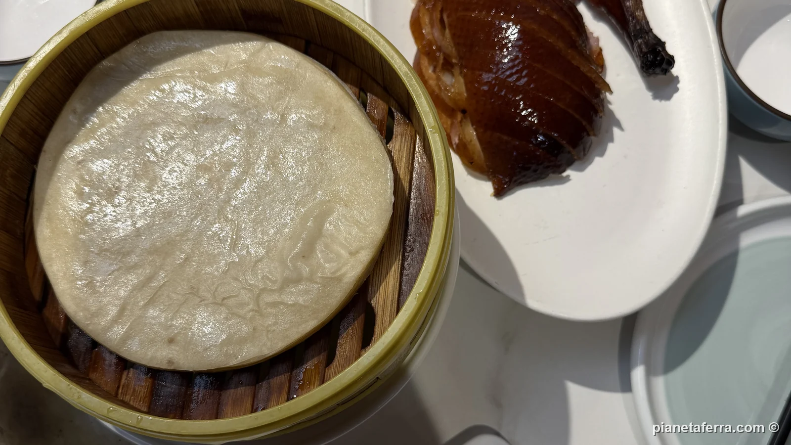 Le crêpe nel cestino di bambù e l'anatra alla pechinese tagliata, a Pechino, a luglio 2026