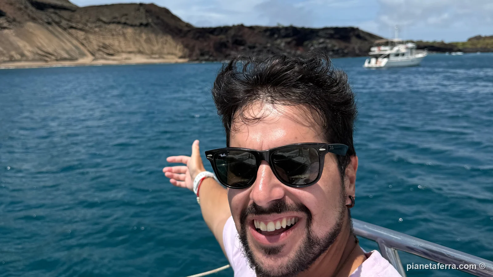 Luca sulla barca della gita di un giorno a Bartolomé, con uno yacht ancorato nella baia, nella primavera del 2025