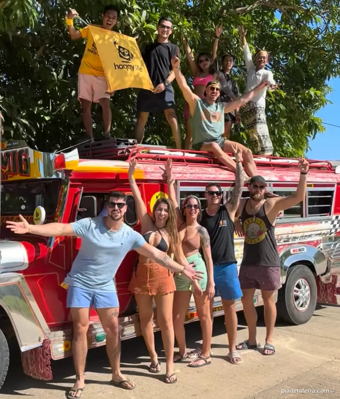 Gruppo di viaggiatori in posa sopra e davanti a una jeepney rossa durante il Jeepney Tour di El Nido