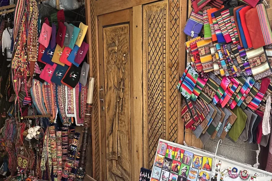 Bancarella di tessuti andini, borse e souvenir davanti a una porta di legno intagliata a La Paz, Bolivia