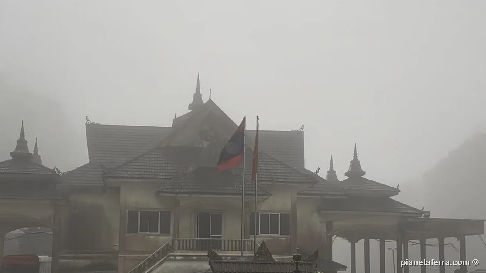 L'ufficio di frontiera laotiano nella nebbia, con la bandiera del Laos, all'ingresso dal Vietnam