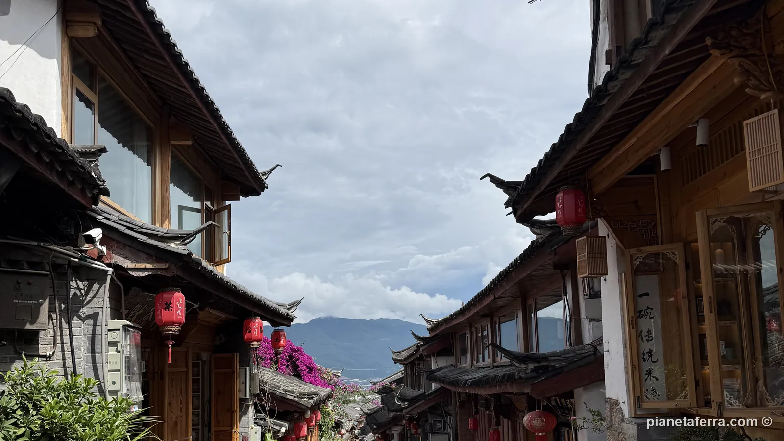 Un vicolo in pietra della città vecchia di Lijiang, con le case di legno Naxi e le montagne in fondo