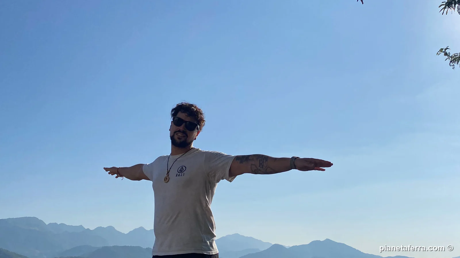 Luca a braccia aperte sulle rocce in cima al Monte Phousi, con le montagne intorno a Luang Prabang