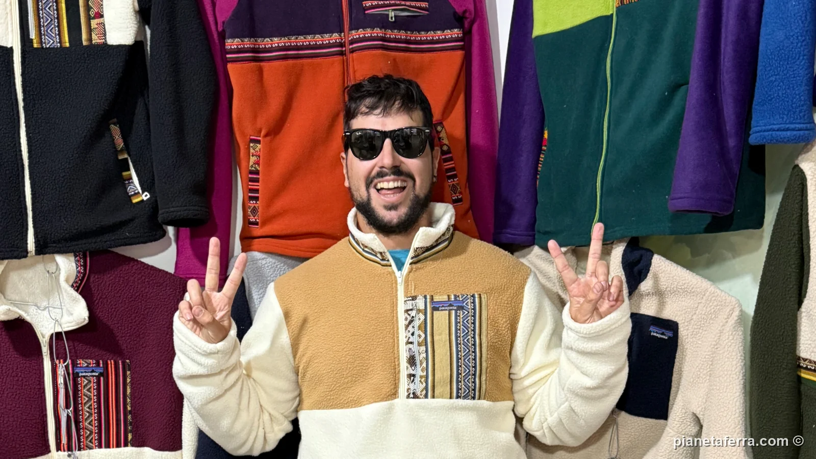 Luca con il pile su misura appena ritirato, beige e bianco con la fascia di aguayo e il logo sul petto, davanti a una parete di pile colorati a La Paz