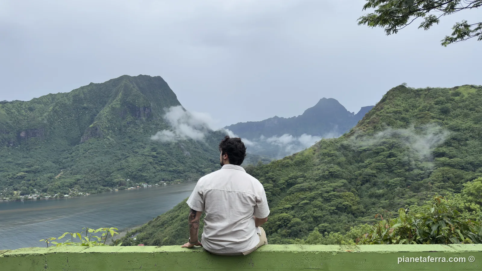 Luca seduto sul parapetto della Magic Mountain, con la baia di Opunohu e le montagne di Moorea tra le nuvole