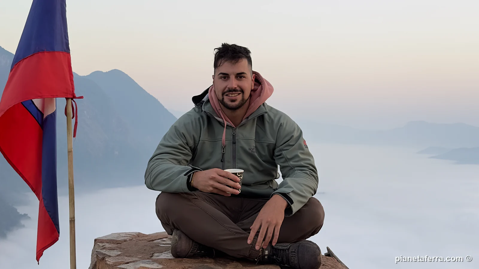 Luca con il caffè e la bandiera del Laos in cima al viewpoint di Nong Khiaw, sopra il mare di nuvole all'alba