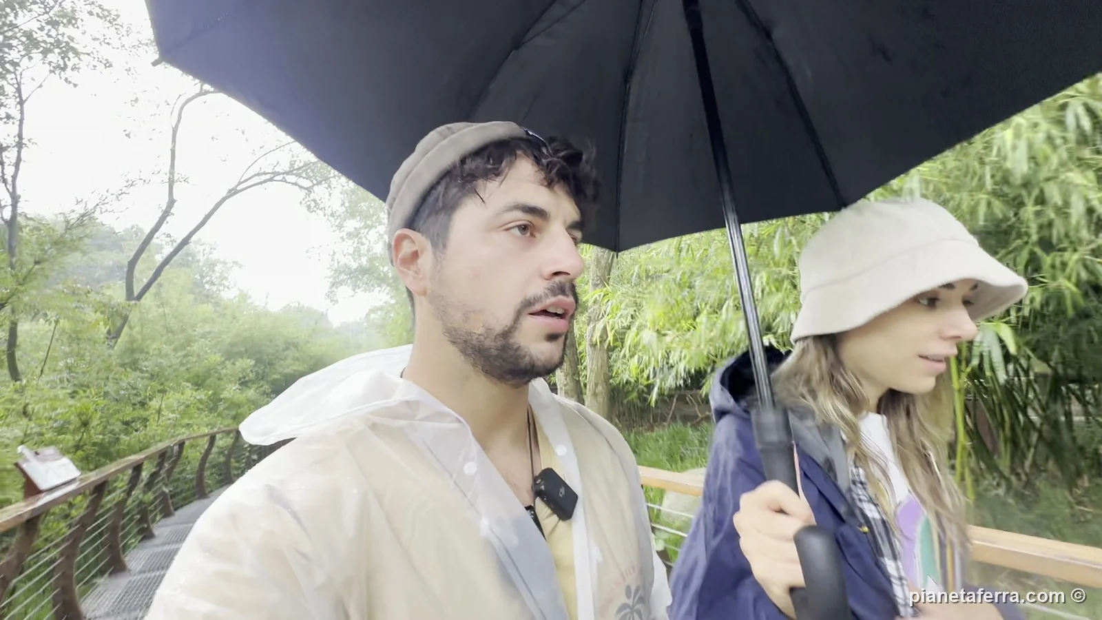 Luca e Patricia sotto la pioggia, con poncho e ombrello, alla base dei panda di Chengdu a maggio 2024