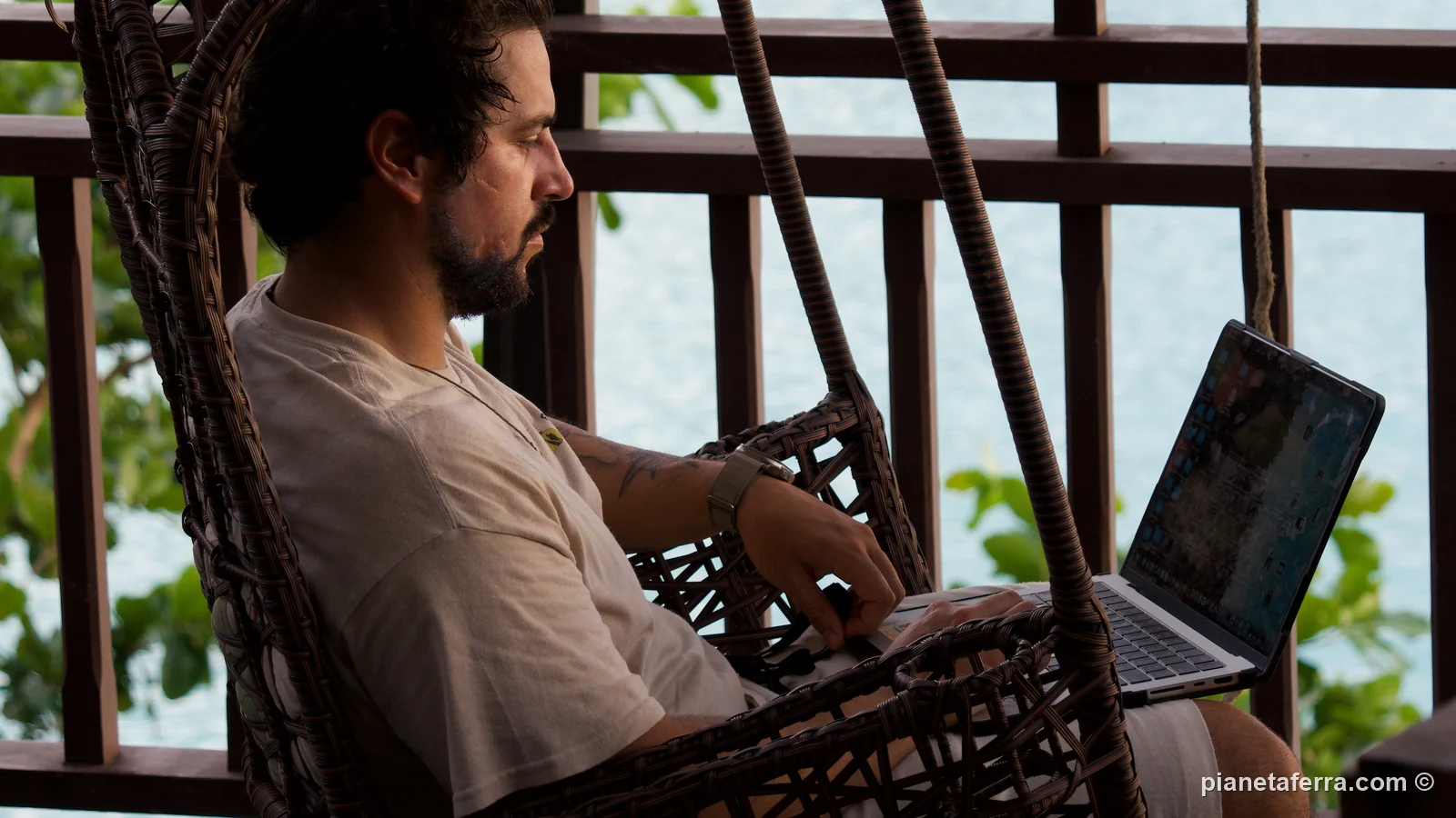 Luca lavora al portatile su una sedia sospesa affacciata su una baia di Phuket