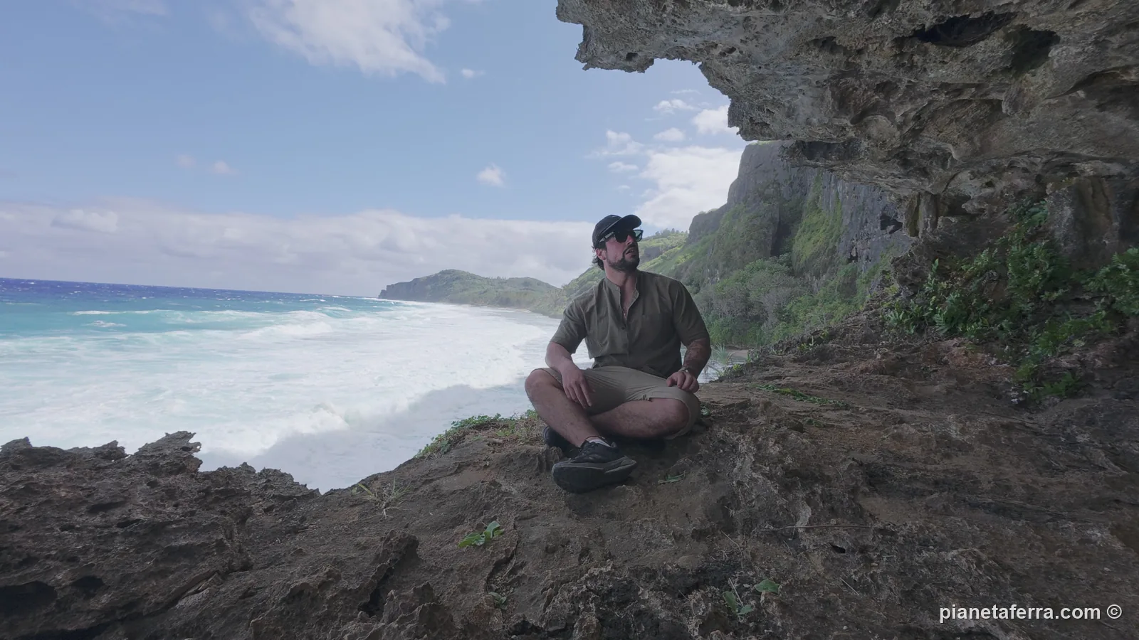 Luca seduto all'ingresso di una grotta a Rurutu, con il mare mosso e le onde bianche sotto, il giorno prima che l'uscita per le balene venisse cancellata