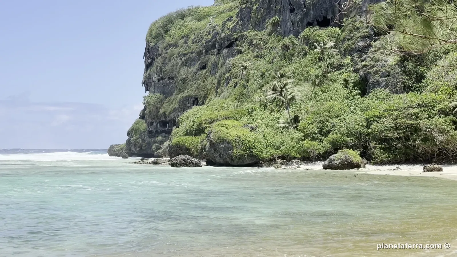Una piccola spiaggia di Rurutu, nelle Isole Australi, sotto una scogliera coperta di vegetazione, con il sole e il vento
