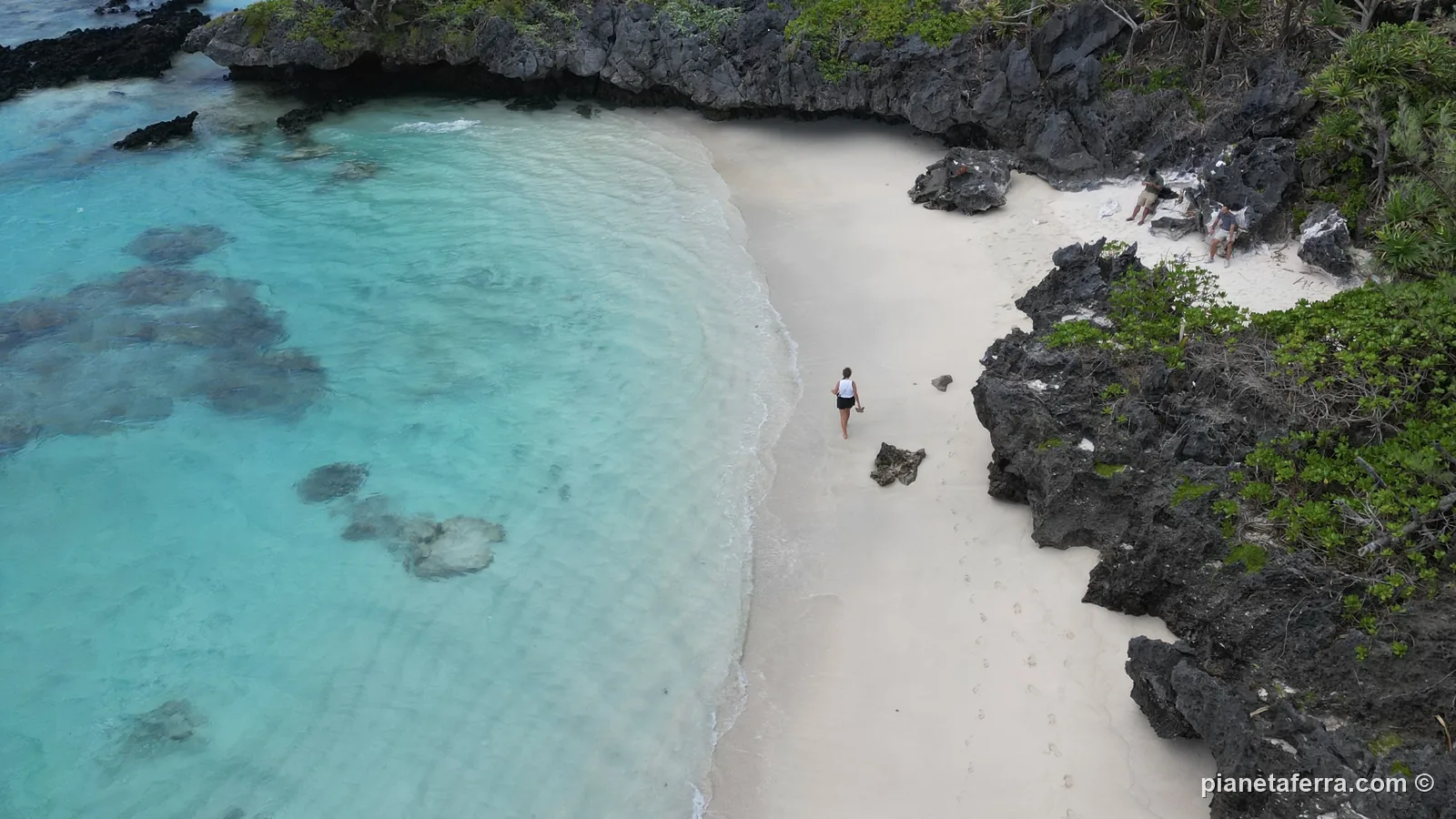 Una spiaggia bianca e vuota di Rurutu tra le rocce scure della scogliera, con l'acqua turchese, vista dal drone