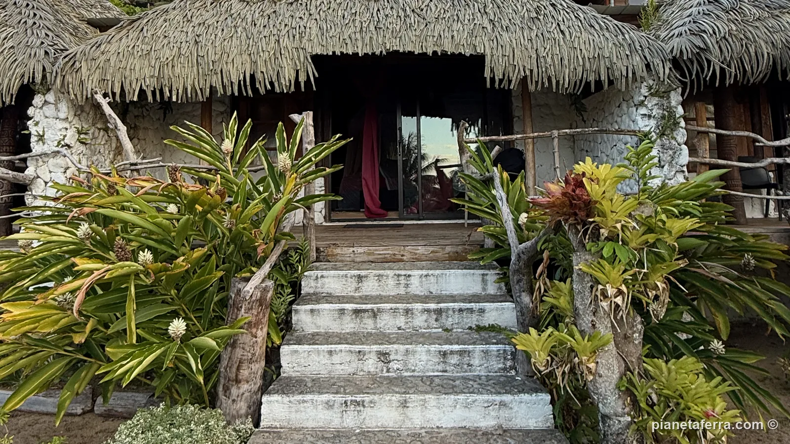 L'ingresso di un bungalow con il tetto di foglie al Vaitumu Village, a Rurutu, tra le piante tropicali
