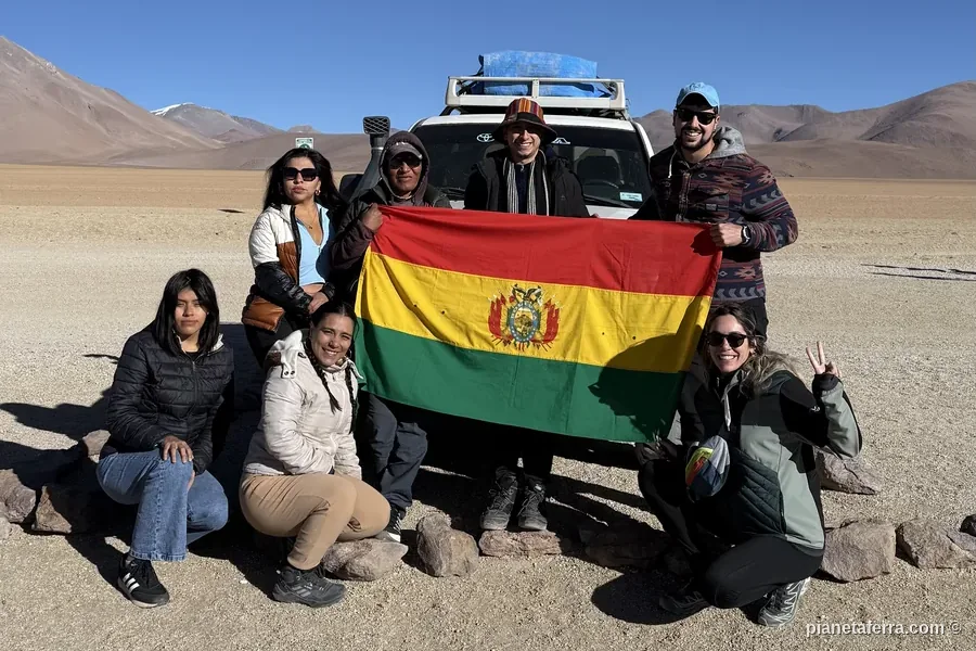 Gruppo di viaggiatori con la bandiera boliviana davanti al 4x4 durante il tour del Salar de Uyuni