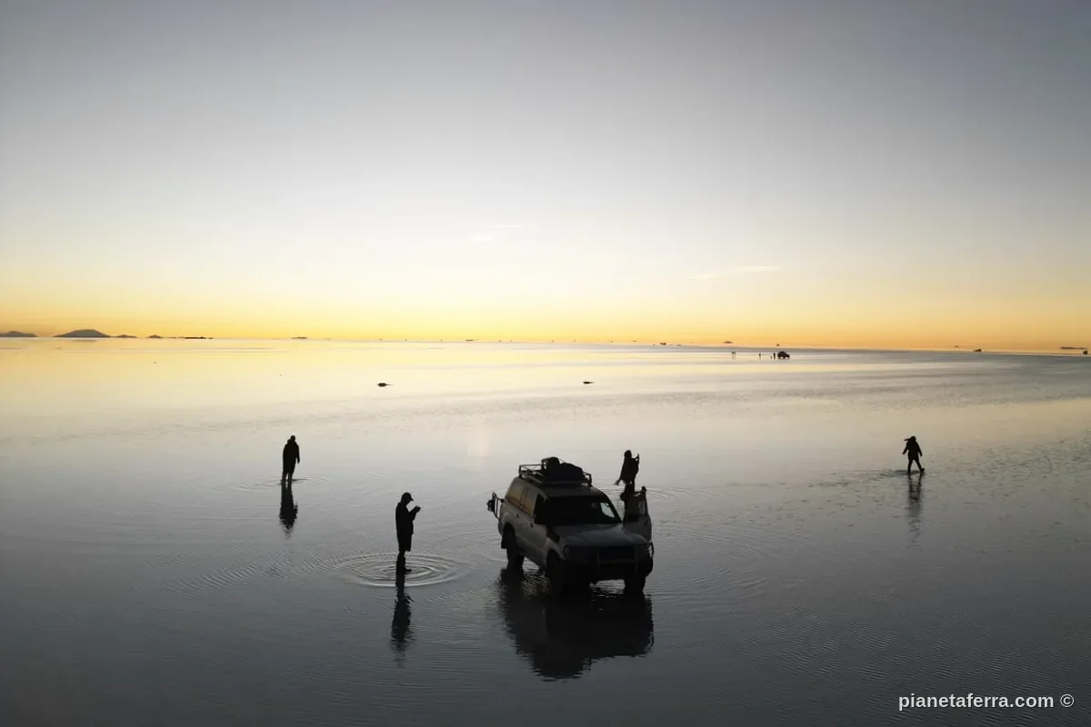 Tramonto sullo specchio d'acqua del Salar de Uyuni con il 4x4 del tour