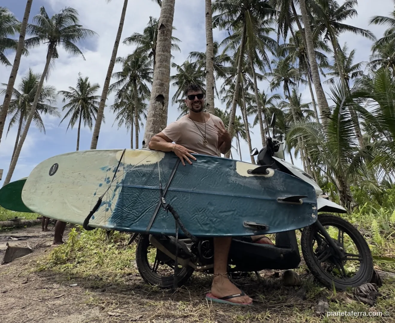 Luca con la tavola da surf appoggiata al motorino tra le palme di Siargao, nelle Filippine