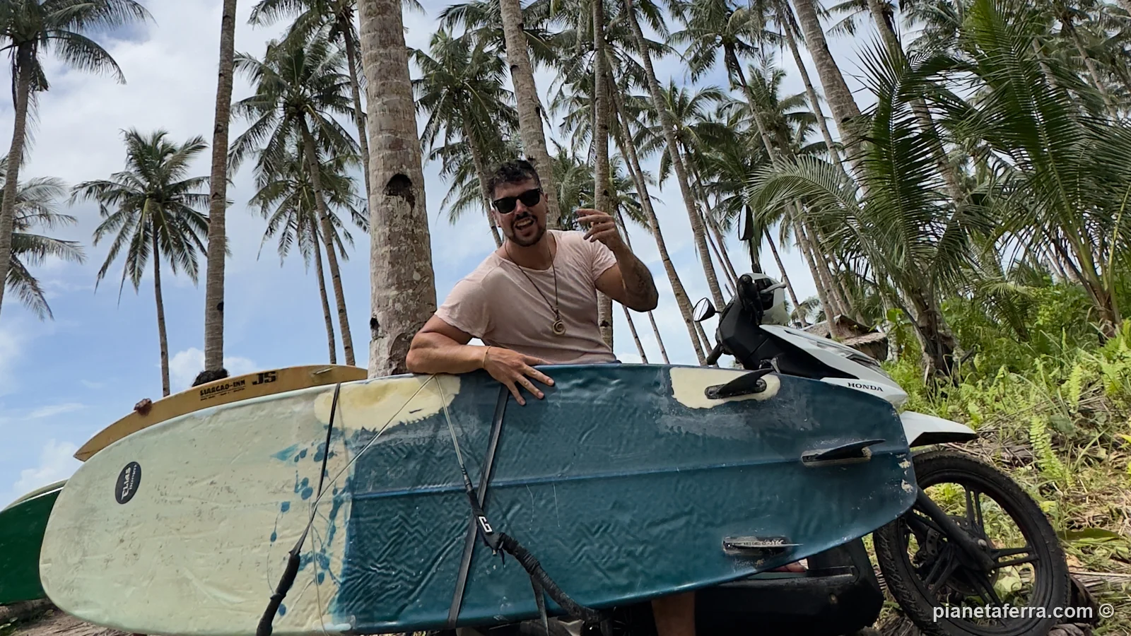 Luca appoggiato alla tavola da surf caricata sul portatavola dello scooter, tra le palme di Siargao, nel 2023