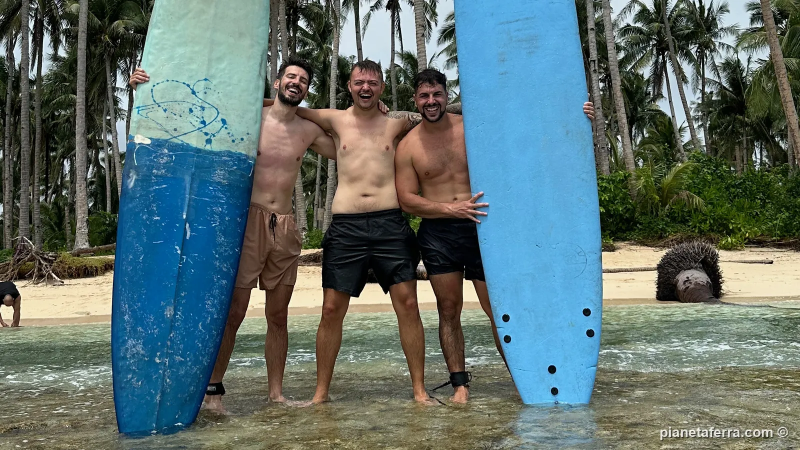 Luca con due amici e le tavole da surf in acqua bassa davanti al palmeto di Siargao, nel 2023