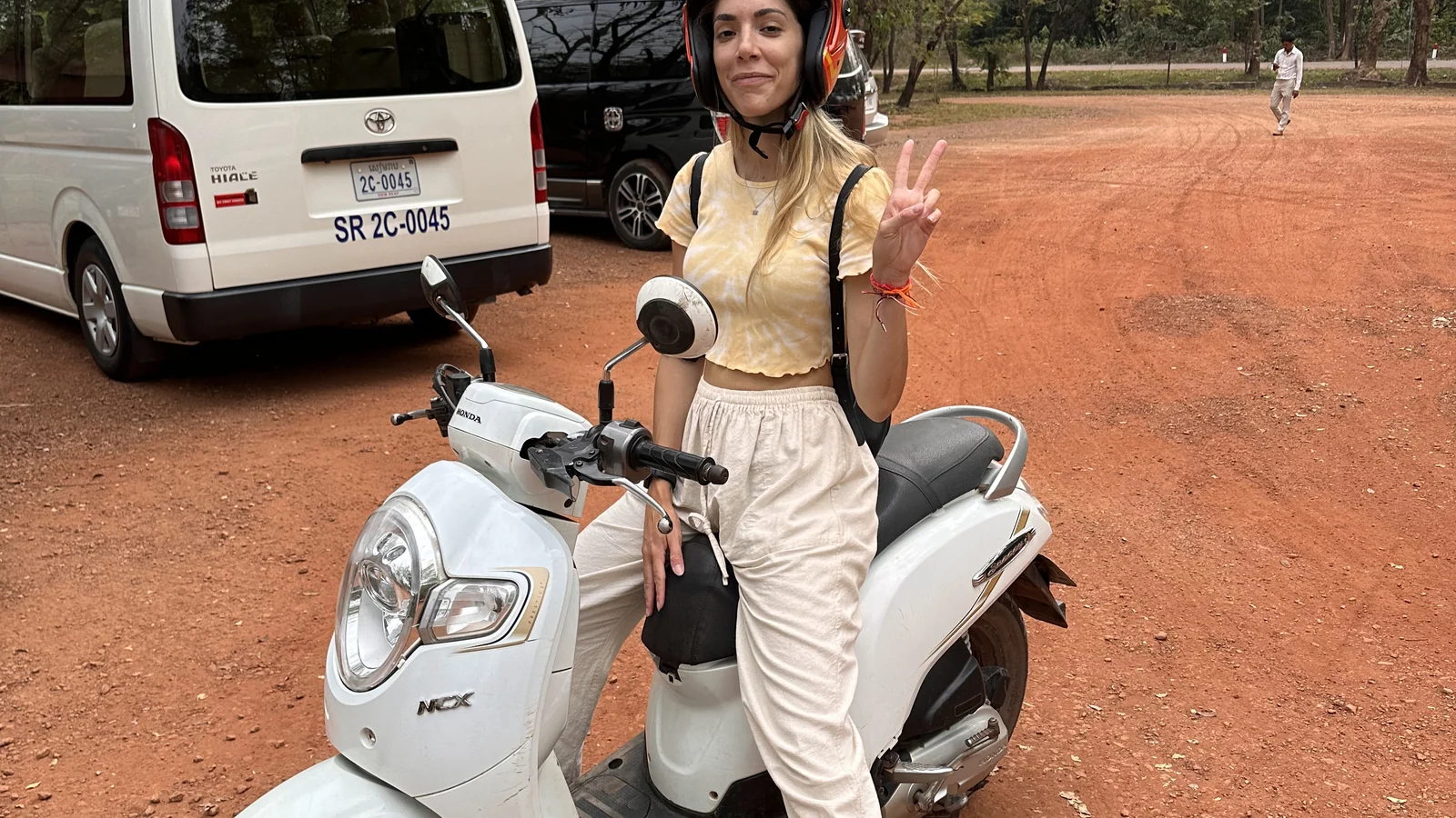 In posa con il casco accanto allo scooter bianco su una strada sterrata del parco di Angkor