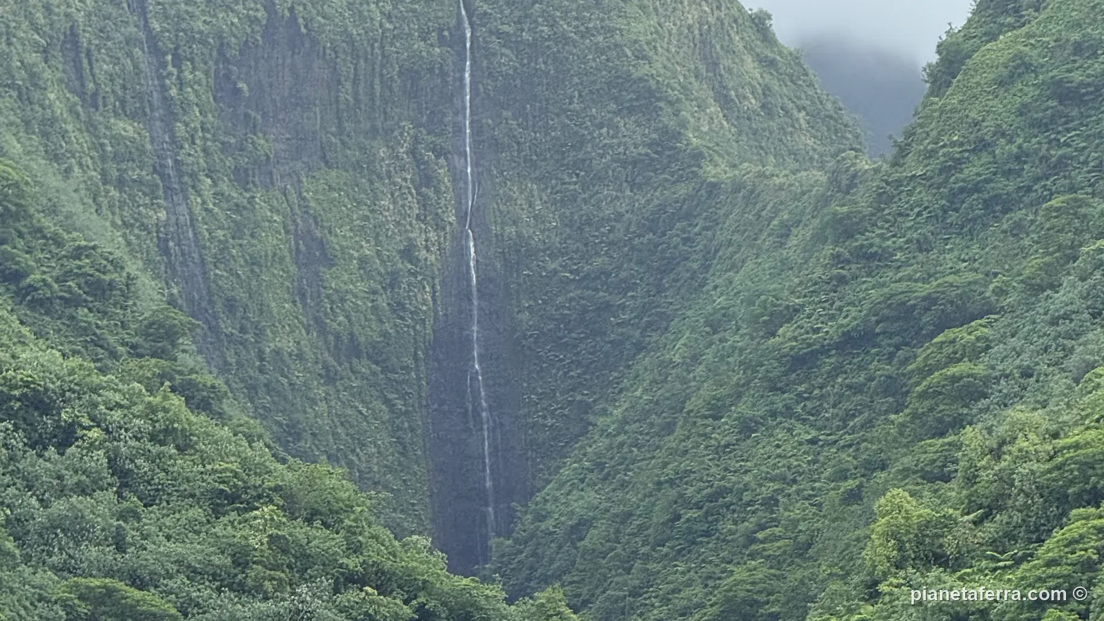 Una cascata altissima che scende in una valle verde di Tahiti Iti, vista dalla barca