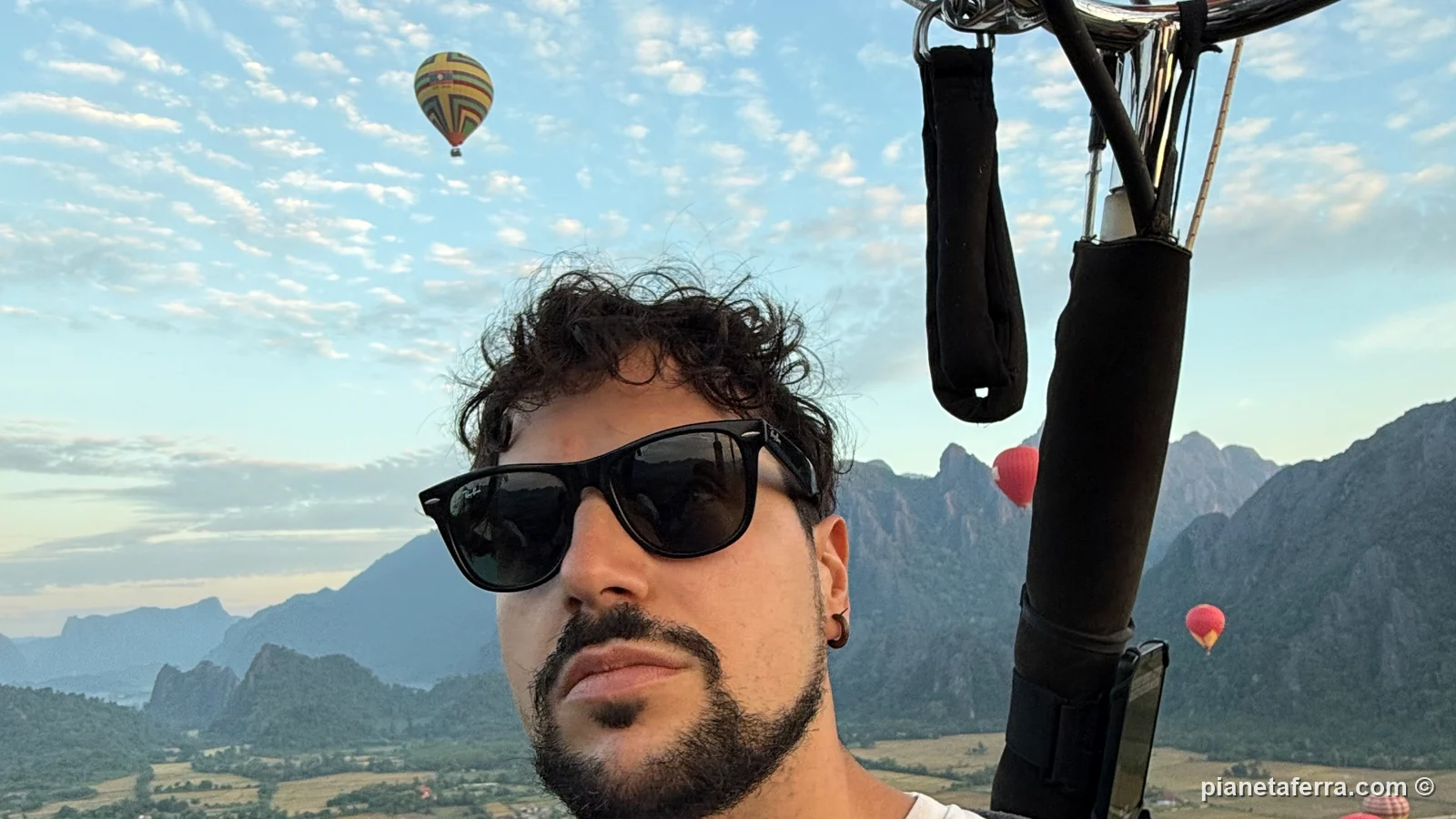 Luca nel cesto della mongolfiera sopra Vang Vieng all'alba, con altre mongolfiere e le montagne carsiche