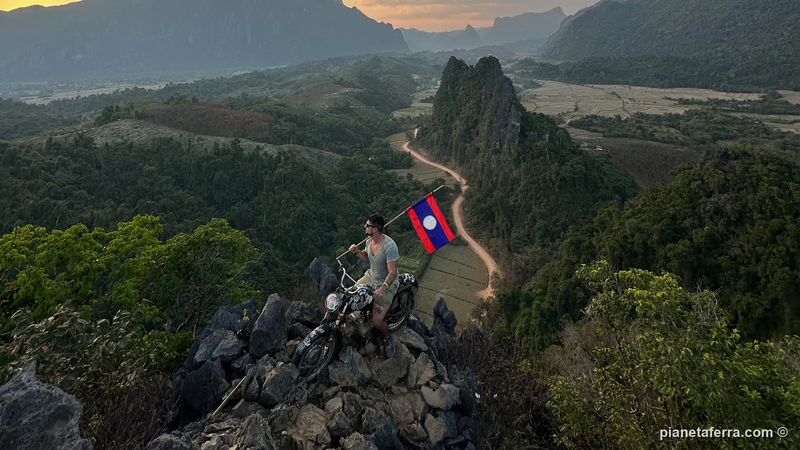 Luca con la bandiera del Laos sulla moto in cima al Nam Xay Viewpoint al tramonto, sopra la valle di Vang Vieng
