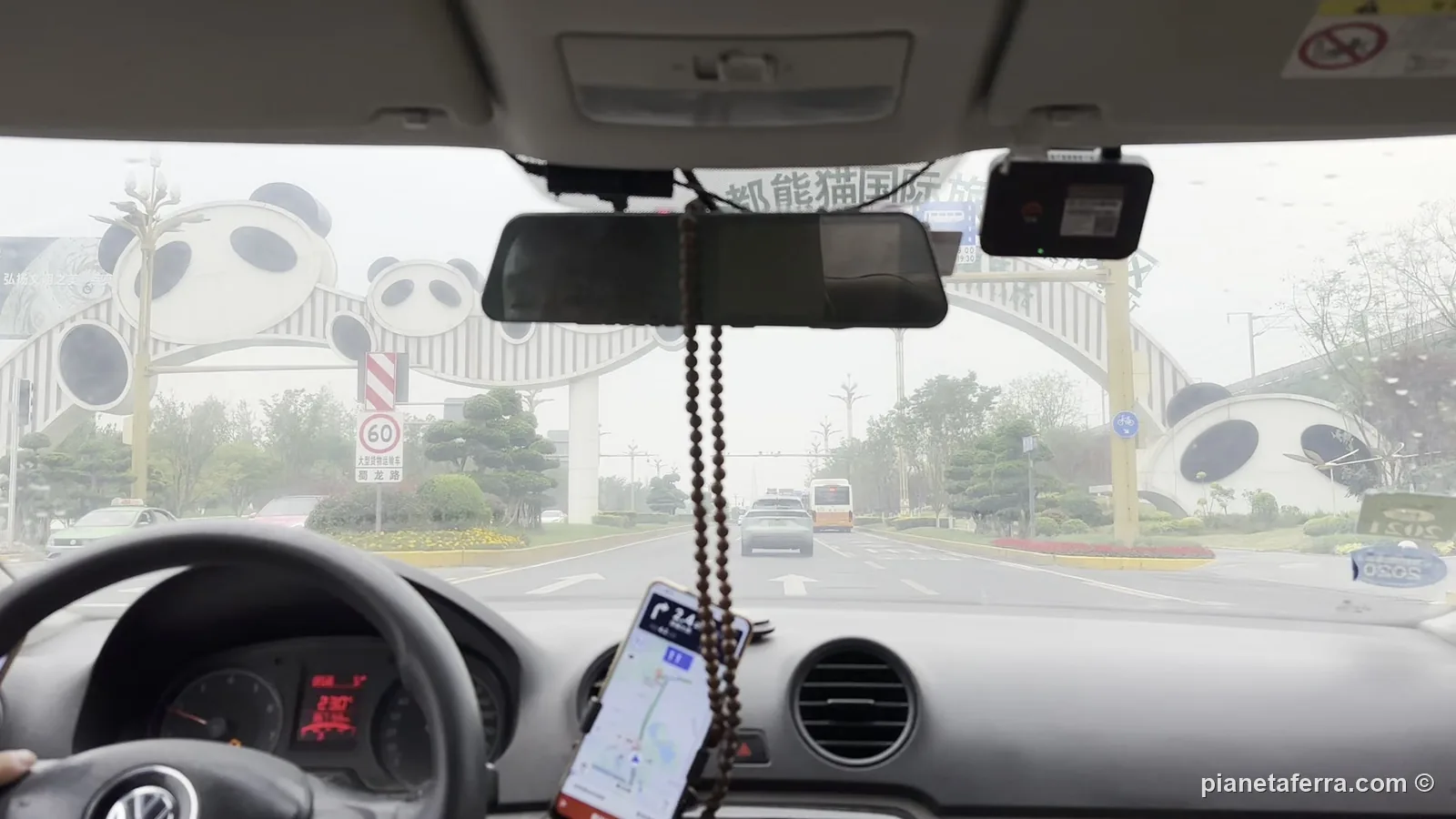 Il telefono con la navigazione sul cruscotto di un DiDi a Chengdu, davanti all'arco con i panda