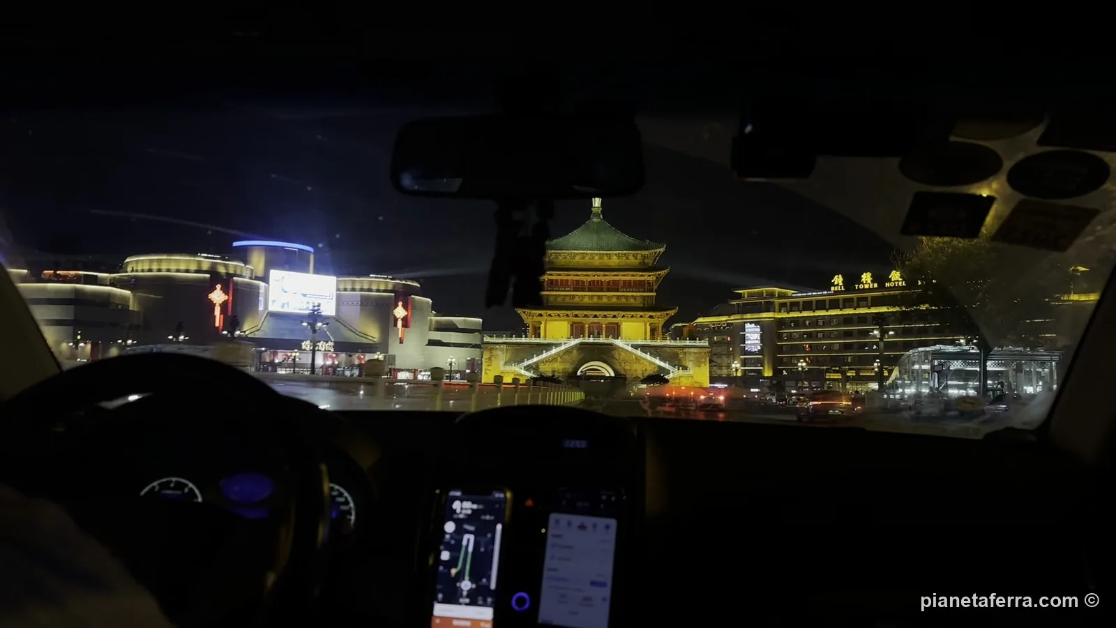 La Torre della Campana di Xi'an illuminata di notte, vista dal taxi con i telefoni sul cruscotto