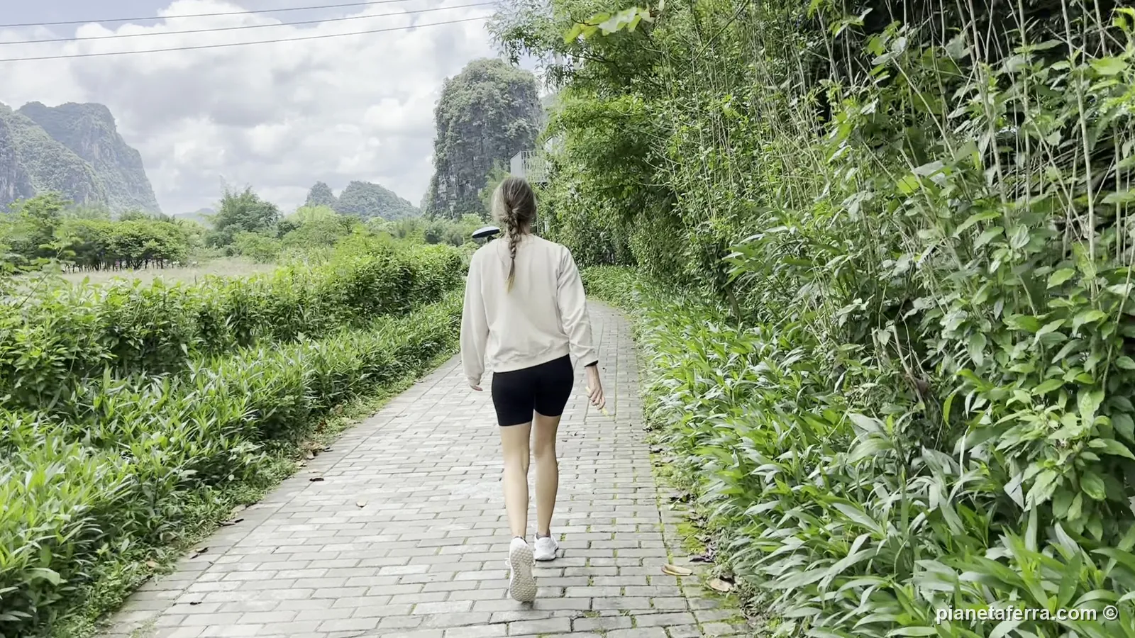 Patricia cammina su un sentiero tra i bambù e i picchi carsici nella campagna di Yangshuo, a maggio 2024